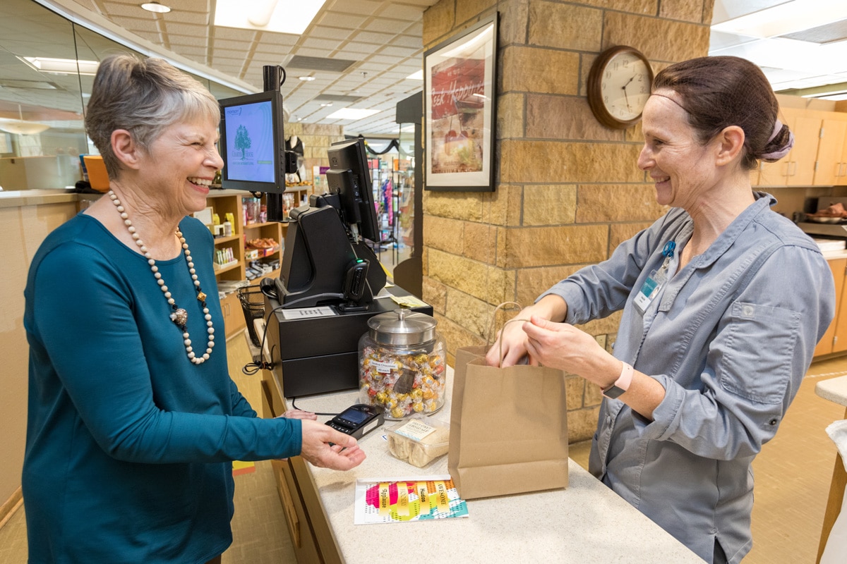 Woman Working In Convenience Store Bagging Residents Purchases Woman Working In Convenience Store Bagging Residents Purchases